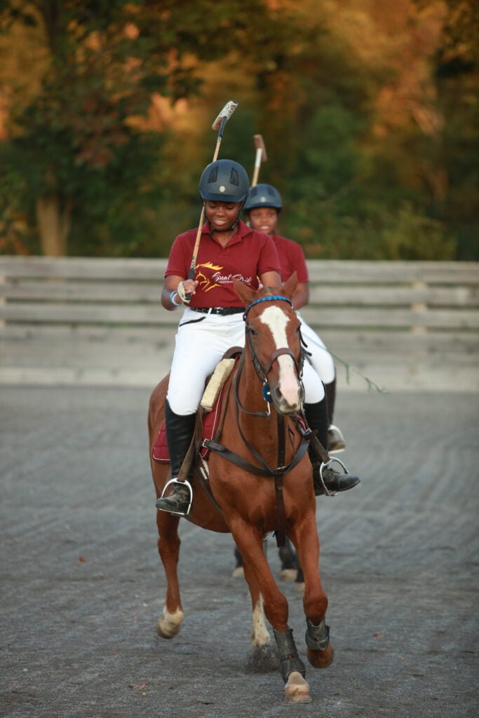 Two young riders on horseback compete in a polo match.